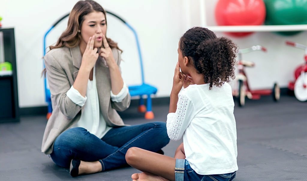 Adult female therapist guiding young girl in speech therapy for a therapy exercise