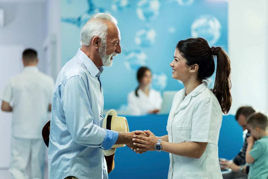 happy senior man handshaking with female doctor while talking in lobby at clinic